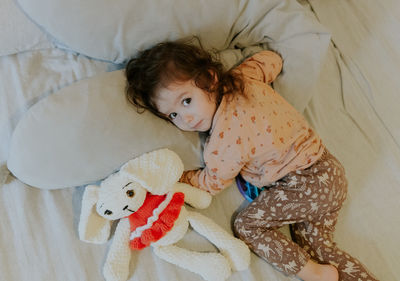 A girl lies on the bed with a toy.