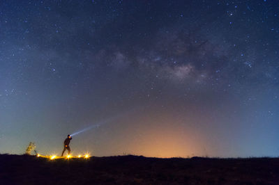 Man with flashlight on field against starry sky