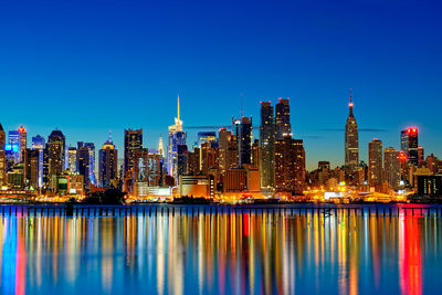 Illuminated buildings in city against clear blue sky