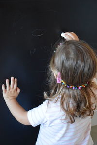 Rear view of girl drawing with chalk on blackboard