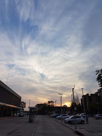 Cars on city street against sky during sunset