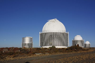 Low angle view of smoke stack on field against clear blue sky