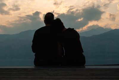 Rear view of couple resting while looking at mountains during sunset