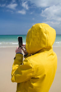 Woman photographing at beach against sky