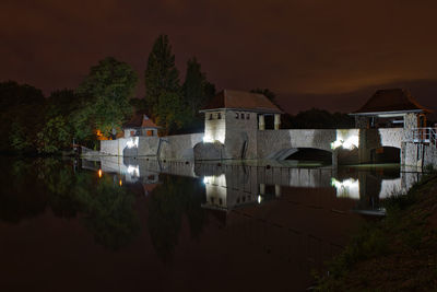 Buildings by lake against sky at night