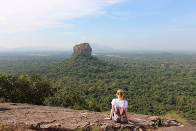 Rear view of woman sitting on mountain against sky