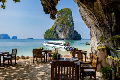 Chairs and table on rocks by sea against sky