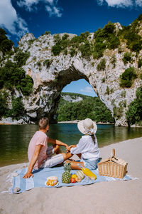 Full length of couple sitting at beach against sky