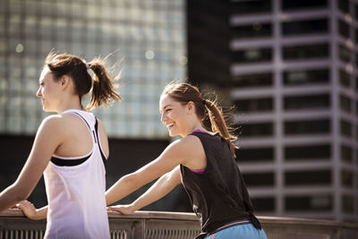 Happy friends standing by railing against buildings