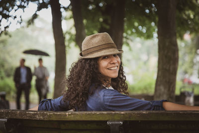 Portrait of smiling young woman wearing hat sitting on bench