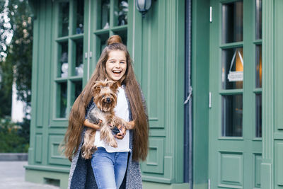 Portrait of happy girl with dog walking by building in city