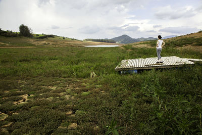 Woman standing on boardwalk at grassy landscape