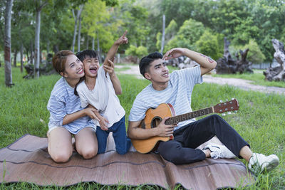 Friends playing guitar while sitting on field
