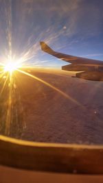 Airplane flying over landscape against sunset sky