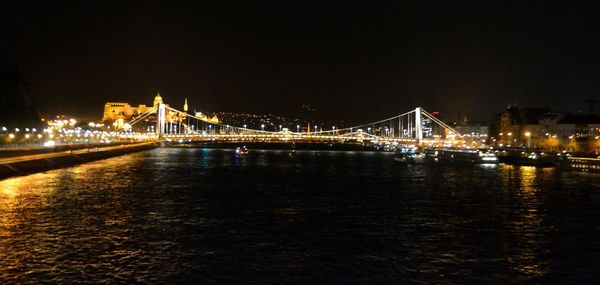 Illuminated bridge over calm river at night