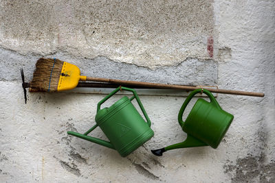 Watering cans and broom hanging on hooks against wall