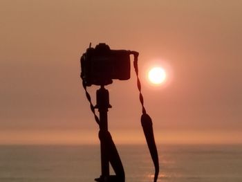 Silhouette camera on beach against sky during sunset