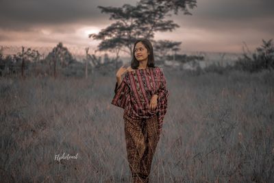 Young woman standing on field against sky during sunset