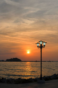 Street light by sea against sky during sunset