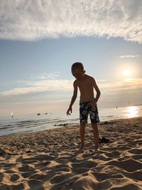 Full length of boy standing on beach against sky during sunset