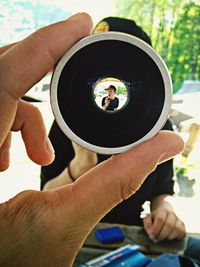 Cropped image man holding camera lens with view of friend