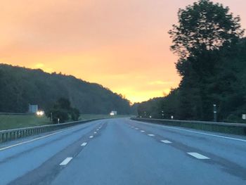 Road by trees against sky during sunset