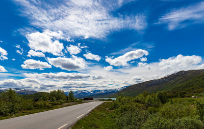 Scandinavian summer afternoon with road and snow capped mountains in the distance under blue skies.