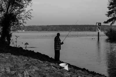 Side view of man fishing at lakeshore against sky