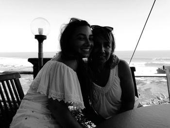 Portrait of happy mother and daughter sitting at cafe against sea