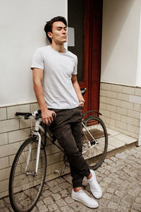 Young man with bicycle standing against door