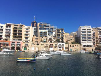 Boats moored at harbor in sea by city against clear blue sky