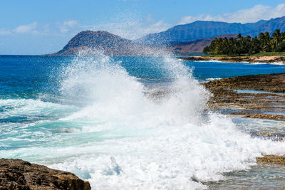 Waves splashing on rocks at shore against sky