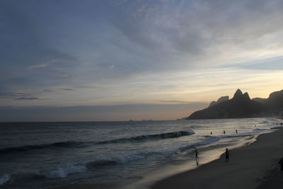 Scenic view of beach against cloudy sky during sunset