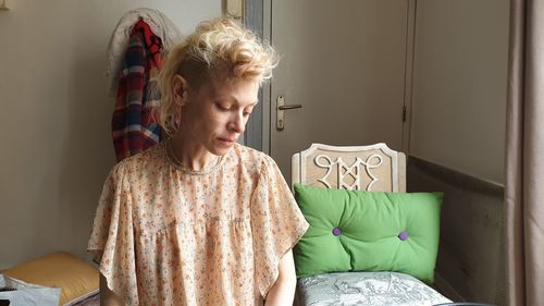 Young woman looking away while sitting on bed at home