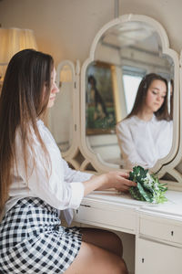 Woman holding bouquet while sitting in front of mirror at home