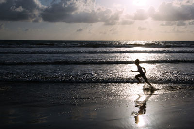 Silhouette man standing on beach against sky during sunset