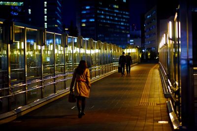 Rear view of woman walking in illuminated city at night