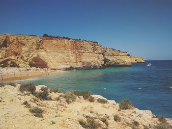 Rock formations in sea against clear blue sky