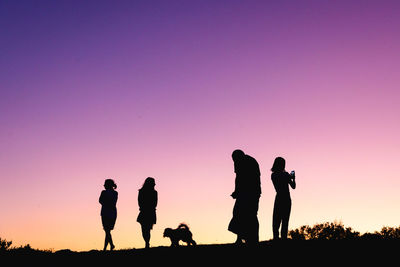 Silhouette people with dogs against sky during sunset