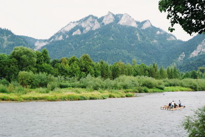People riding boat on river against mountains
