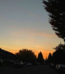 Cars on street against sky at sunset