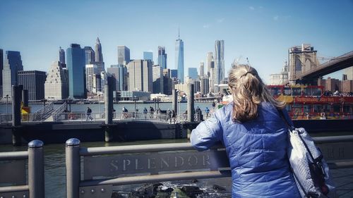 Rear view of woman standing by railing in city against sky