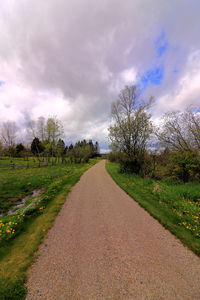 Dirt road amidst field against sky