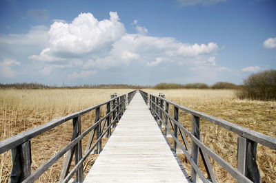 Wooden footbridge on field against sky