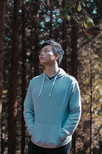 Portrait of young man standing against trees in forest