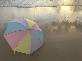 Colorful pastel umbrella putting on clear beach with sea wave, cloud shadow and golden sunlight