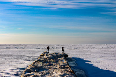 People on shore during winter against sky