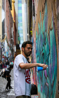 Side view of young man standing against wall in city