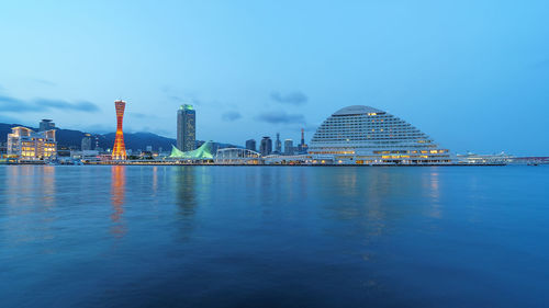 Illuminated buildings in city against clear blue sky