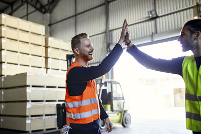 Happy colleagues in protective workwear high fiving in factory